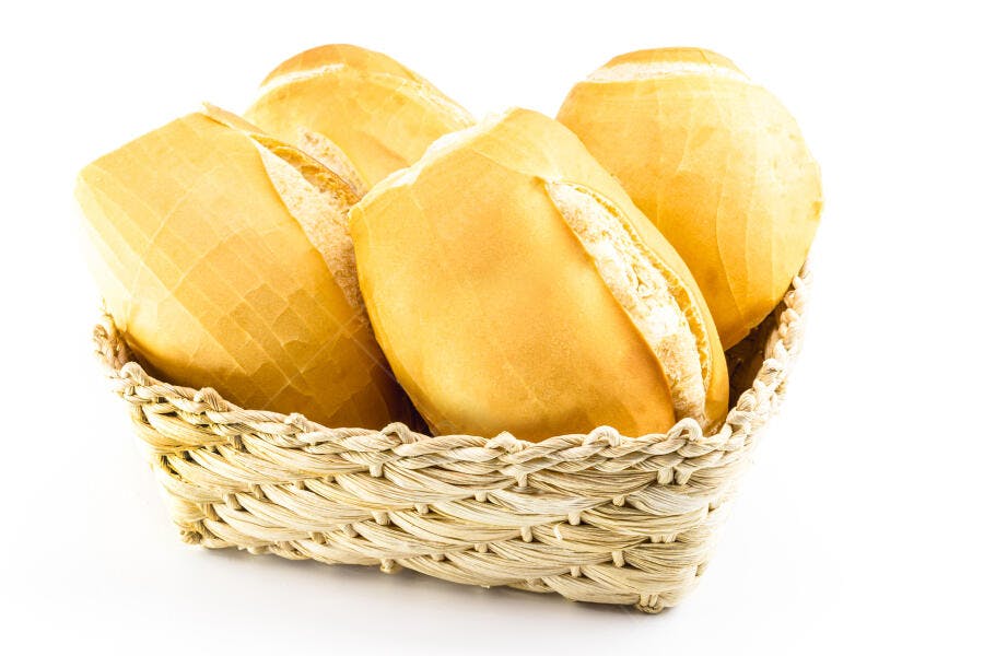 Pães franceses dourados em cesta de vime sobre fundo branco
