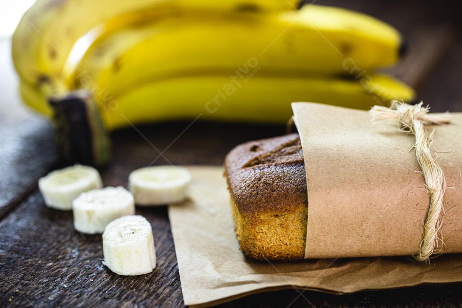 Bolo de banana fresco embrulhado com bananas amarelas e fatias em mesa rústica