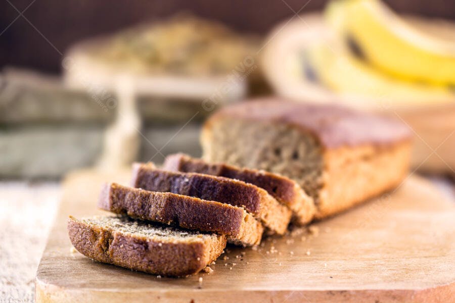 Pão de banana fatiado em tábua de madeira rústica com bananas no fundo