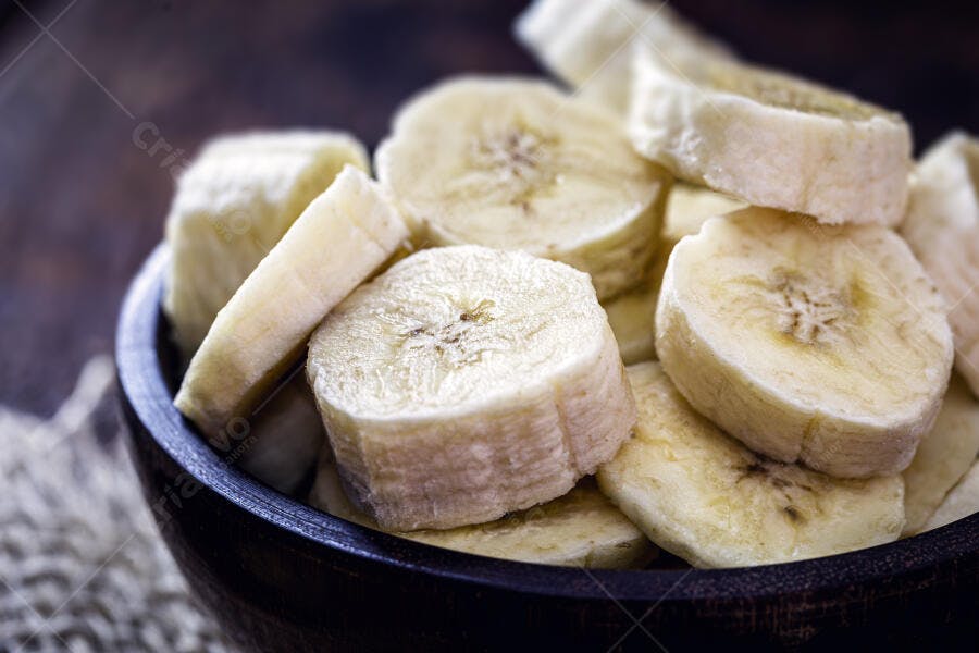 Bananas fatiadas frescas em tigela de madeira escura para lanche saudável