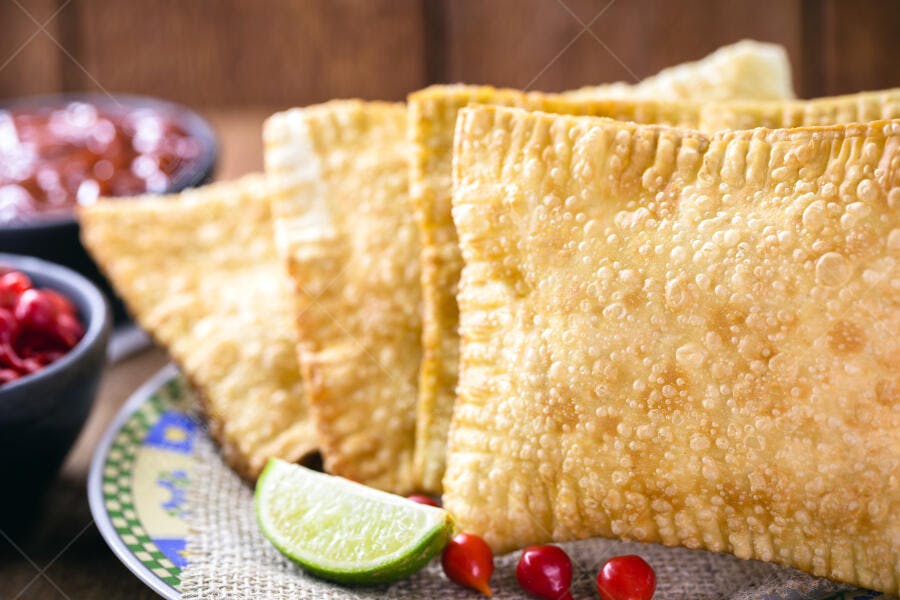 Pastéis crocantes de feira com limão e pimenta biquinho em mesa rústica