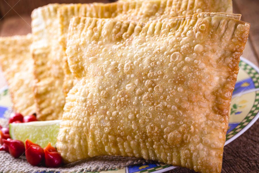 Pastéis fritos dourados crocantes com pimenta biquinho e limão em prato rústico