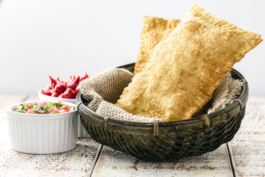 Pastéis fritos dourados e crocantes em cesto com pimenta e vinagrete na mesa rústica