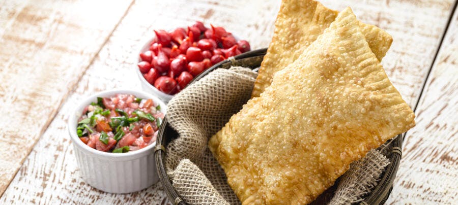 Pastéis brasileiros dourados crocantes com vinagrete e pimenta biquinho em mesa rústica