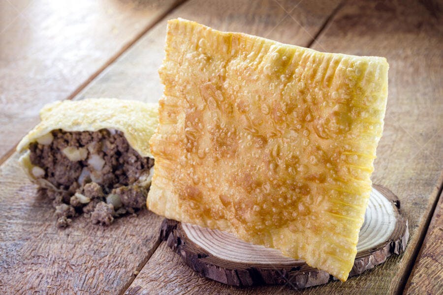 Pastel de carne frito dourado com recheio de carne moída e batata na mesa de madeira