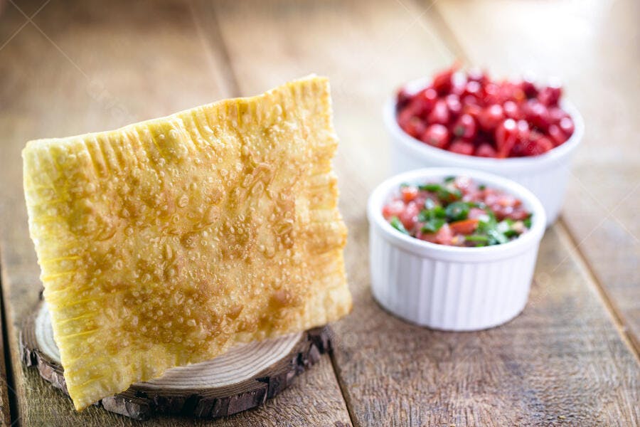Pastel frito dourado em mesa de madeira rústica com molhos