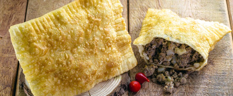 Pastéis de carne fritos crocantes um aberto com pimenta vermelha em mesa de madeira rústica