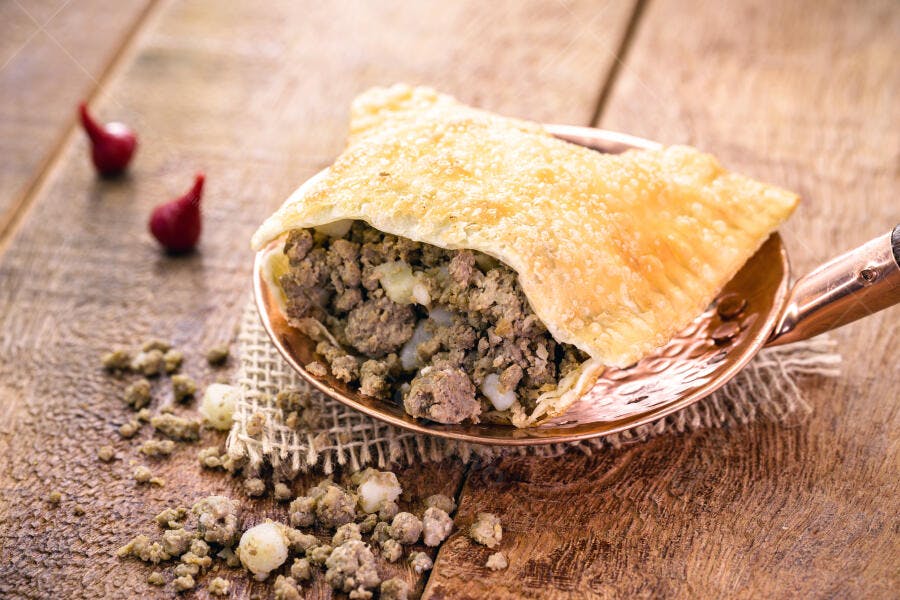 Pastel de carne moída aberto em colher de cobre sobre mesa de madeira rústica