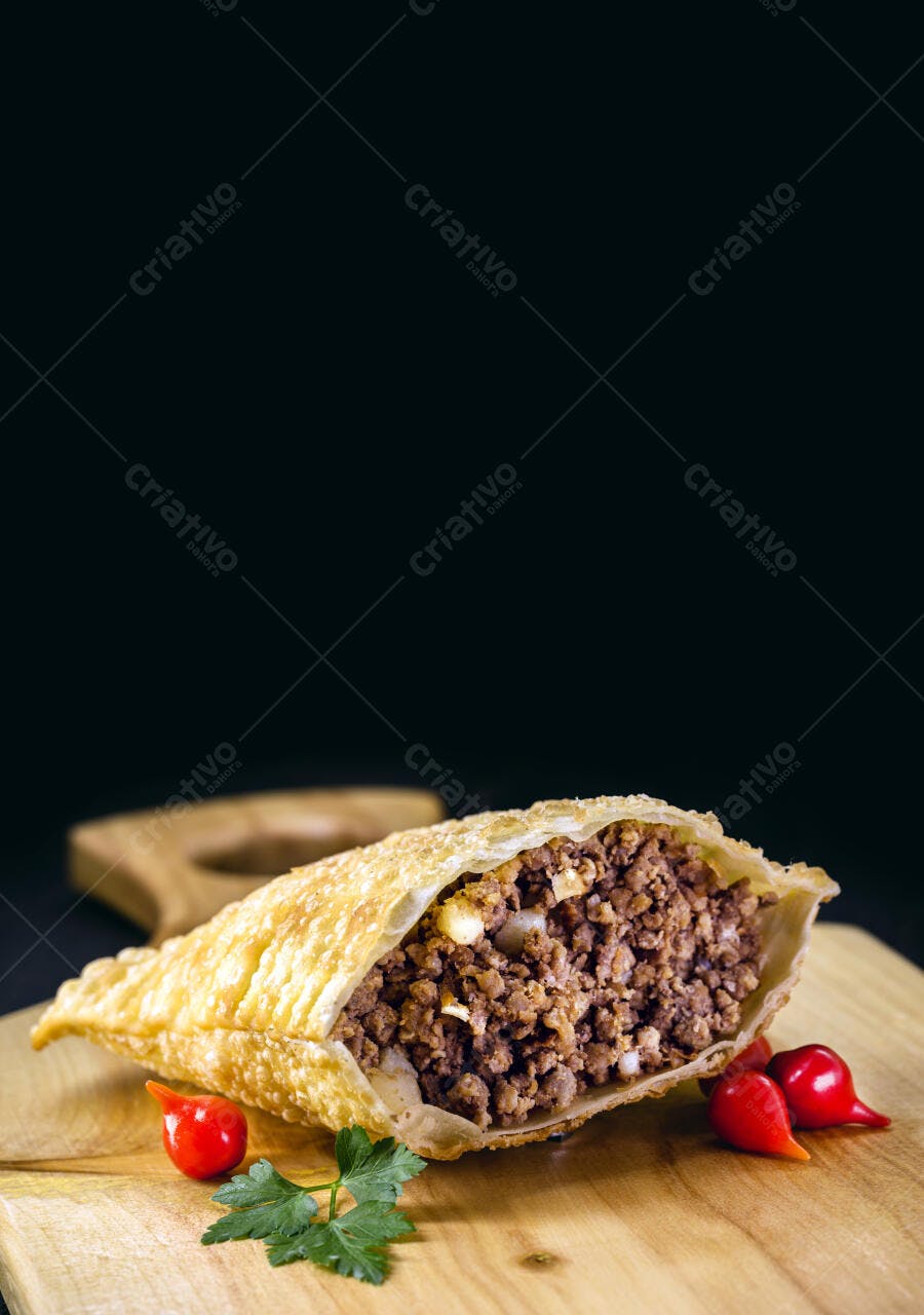 Pastel de carne frito aberto com pimenta biquinho e salsinha em tábua de madeira