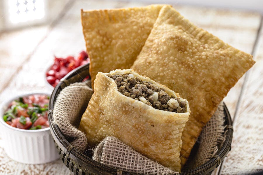 Pastéis de carne fritos em cesta rústica com vinagrete e pimenta