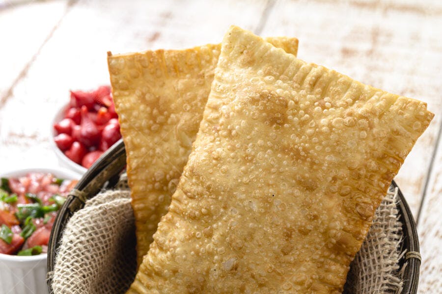Pastéis fritos dourados crocantes em cesta rústica com pimentas e vinagrete