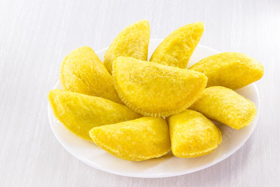 Empanadas amarelas fritas servidas em prato branco para lanche