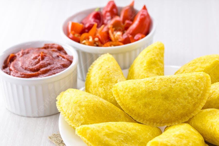 Empanadas amarelas com molho de tomate e pimentas vermelhas frescas