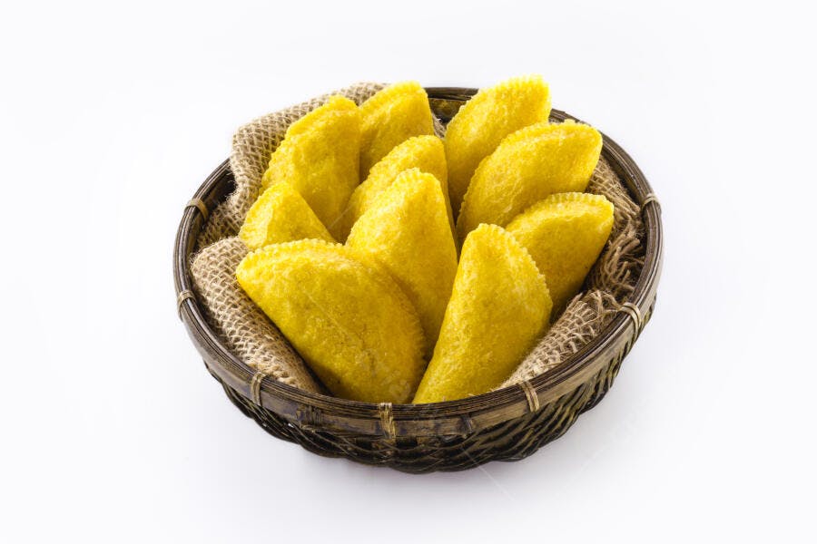 Empanadas amarelas em cesta de vime com fundo branco