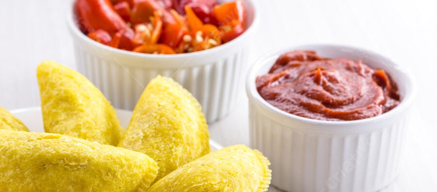 Empanadas fritas douradas com molho vermelho e pimentões em tigelas brancas