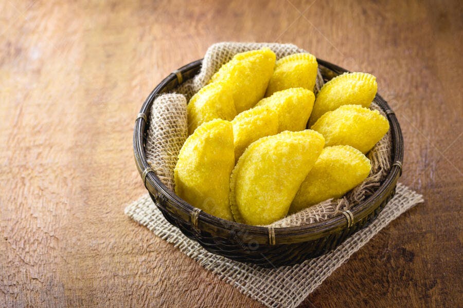 Pastelitos amarelos fritos em cesta rústica de madeira
