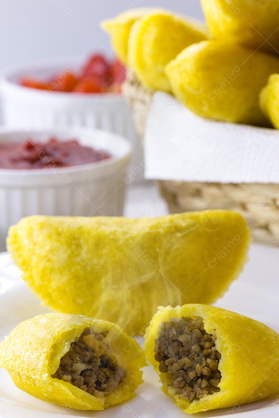 Empadas de carne amarelas com recheio em prato branco e molhos ao fundo