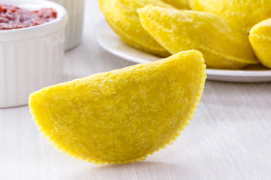 Pastel frito salgado amarelo dourado com molho vermelho em fundo branco