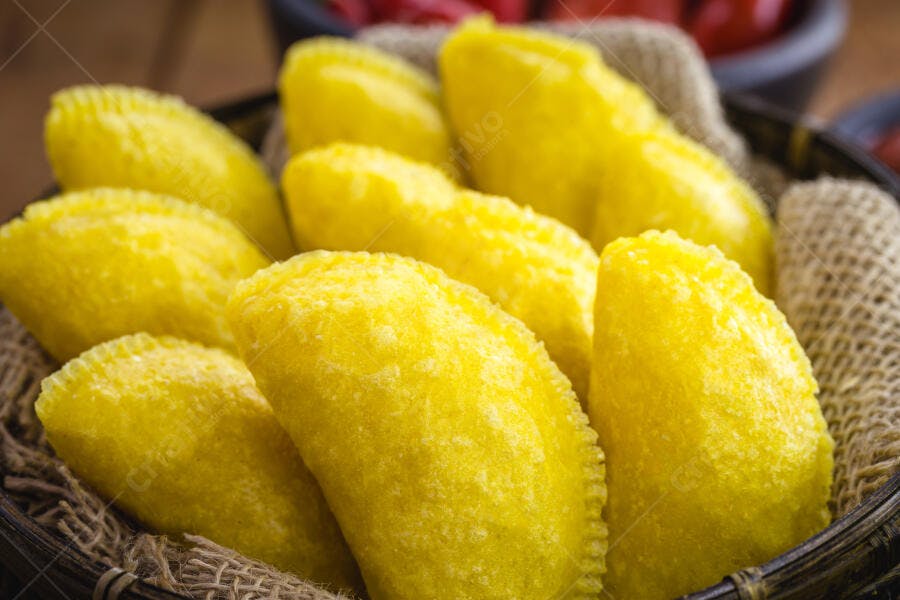 Pastéis amarelos fritos em cesto rústico com bordas detalhadas e fundo de madeira