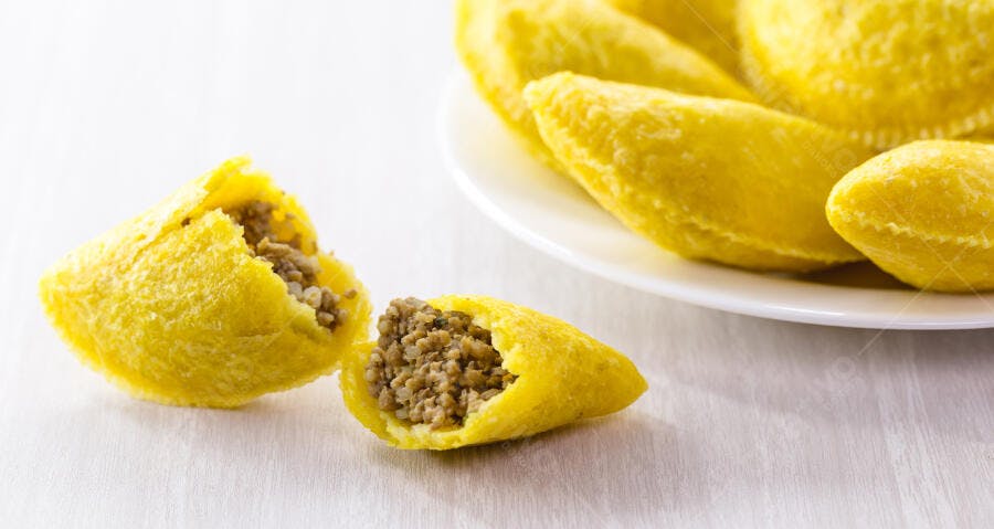 Empanadas amarelas recheadas com carne e arroz em mesa branca