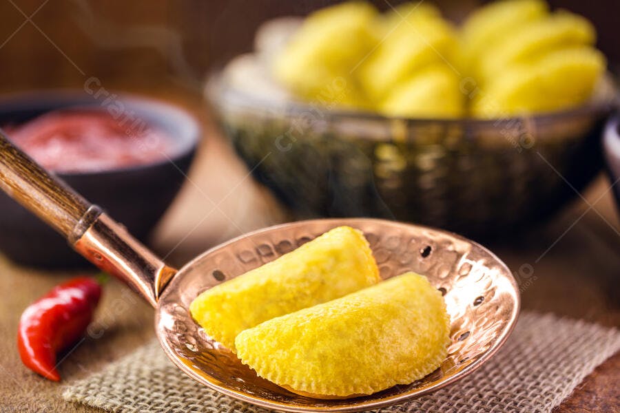 Pastéis fritos dourados em travessa de cobre com molho e pimenta