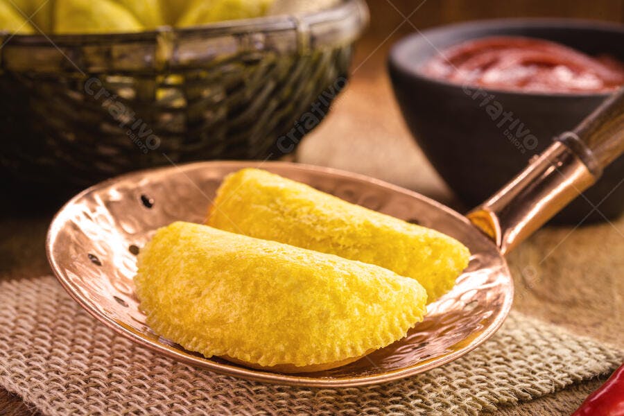 Dois pastéis fritos dourados em frigideira de cobre com molho vermelho e pimenta