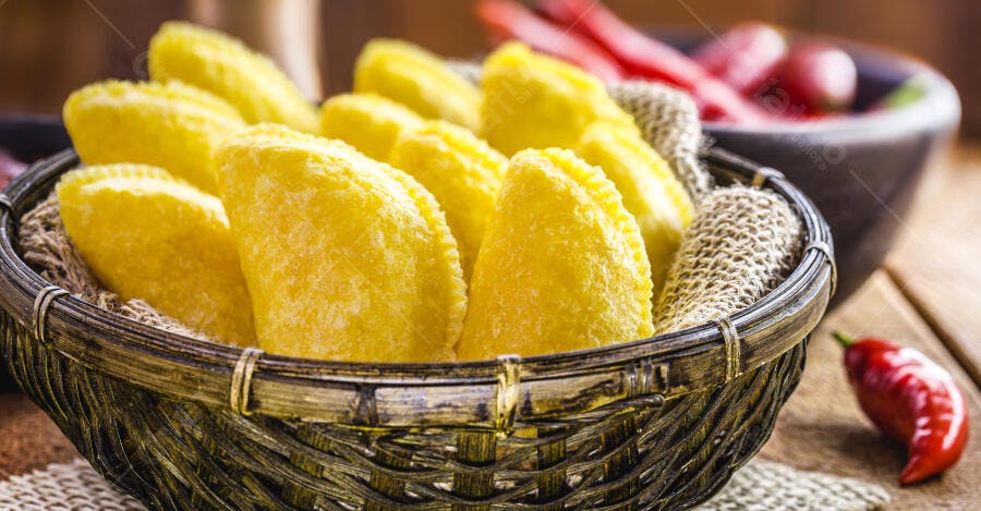 Pastéis fritos amarelos dourados em cesta de vime com pimentas vermelhas