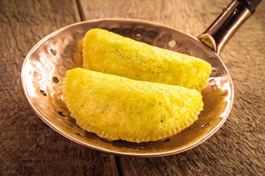 Pastéis amarelos fritos em panela de cobre sobre madeira rústica