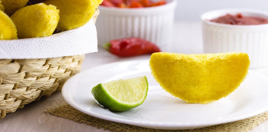 Pastel frito de milho amarelo com limão em mesa branca