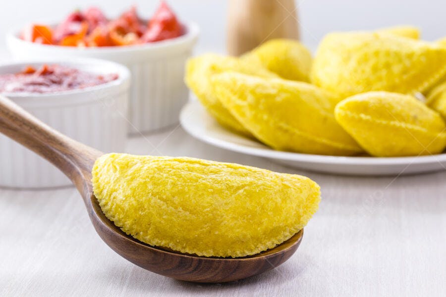 Empanada de milho amarela em colher de madeira com molhos picantes