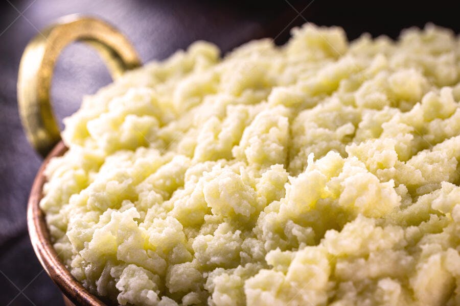 Purê de batata cremoso em tigela rústica com alça dourada e fundo escuro