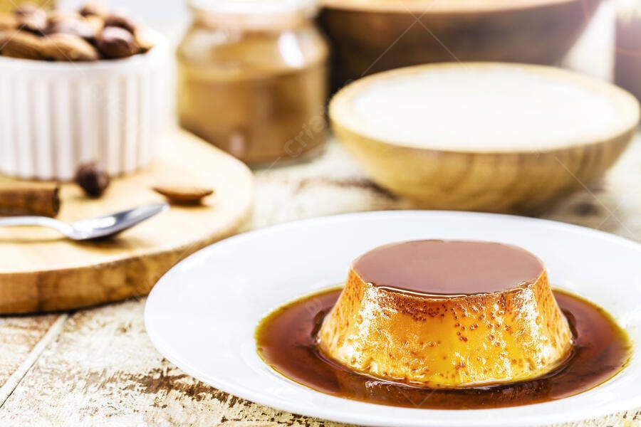 Pudim de leite com calda de caramelo em mesa de madeira com amêndoas