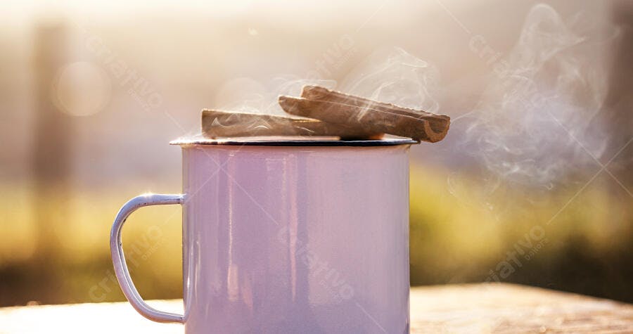 Caneca esmaltada branca com vapor e paus de canela em amanhecer dourado