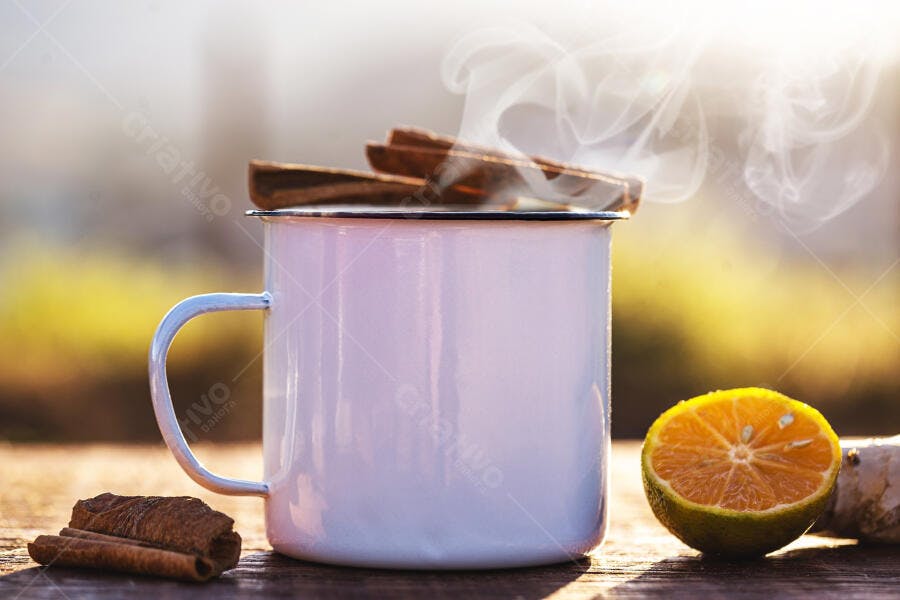 Caneca fumegante com canela e laranja em mesa de madeira ao sol