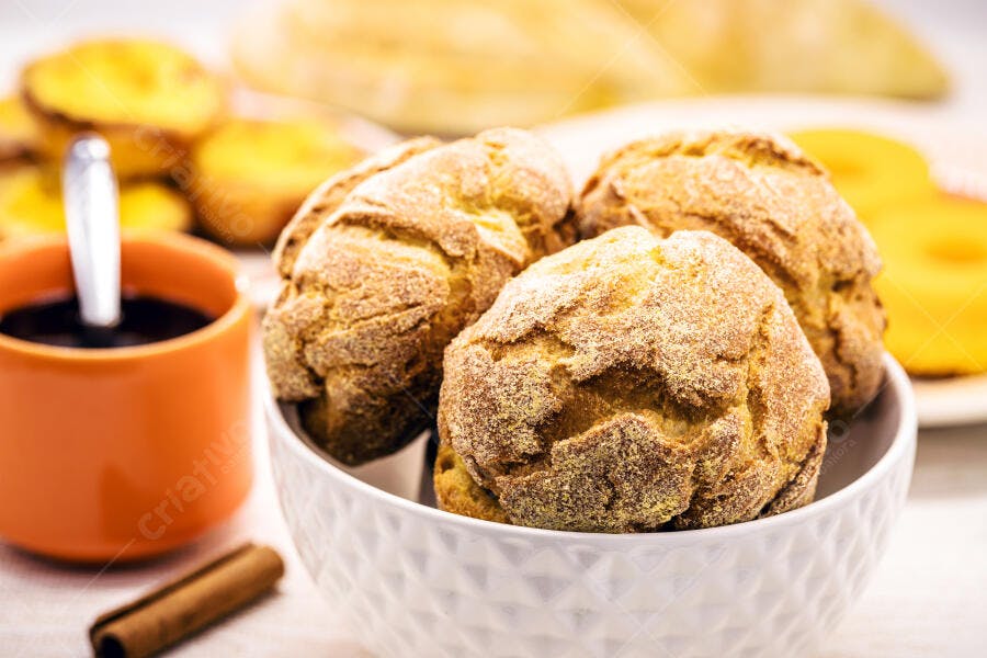 Pão de queijo dourado e crocante com café em xícara laranja e canela