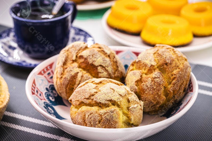 Pães de queijo dourados em tigela decorada servidos com café e quindim