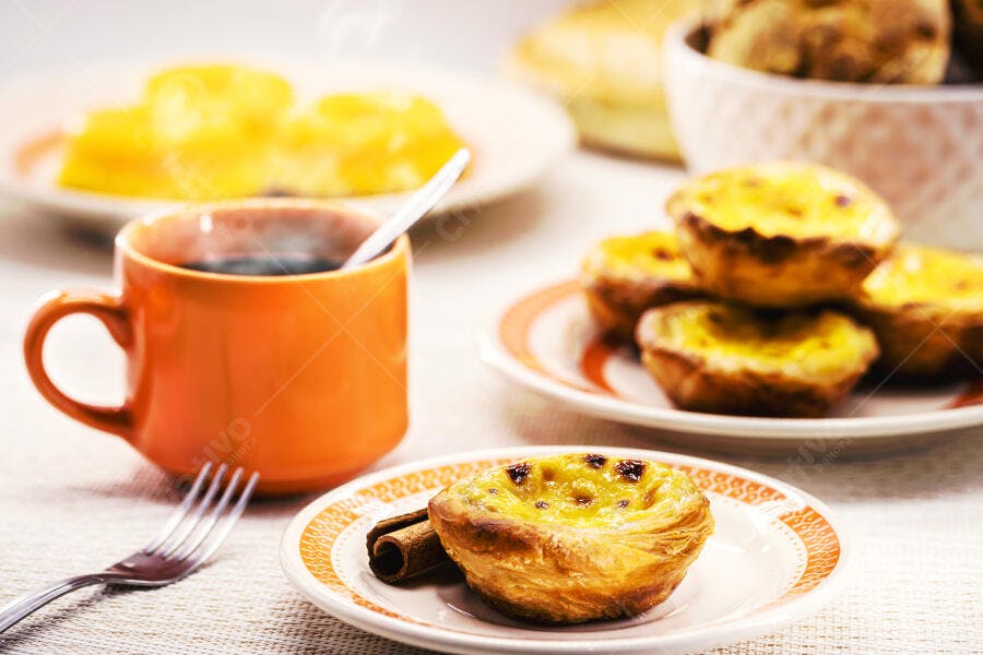 Pastel de Nata e café quente em caneca laranja com canela em mesa de café