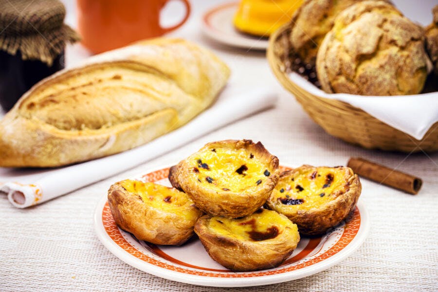 Pastéis de nata dourados e pães frescos em mesa de café da manhã