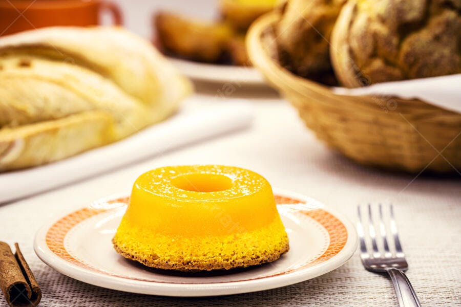 Quindim cremoso amarelo em prato com pão e canela na mesa