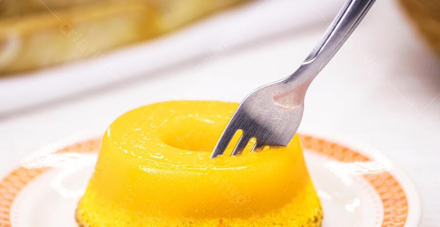 Pudim de coco amarelo vibrante sendo provado com garfo em prato branco