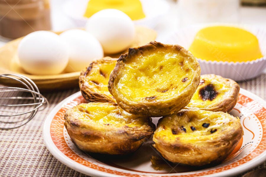 Pastéis de nata frescos em prato com ovos e utensílios de cozinha