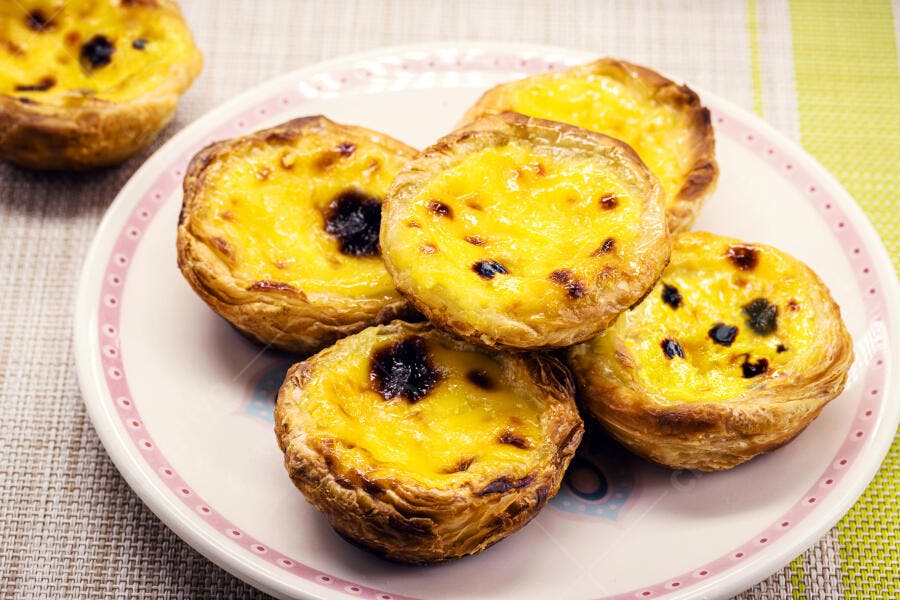 Pastéis de Nata amarelos e crocantes em prato branco com detalhe rosa
