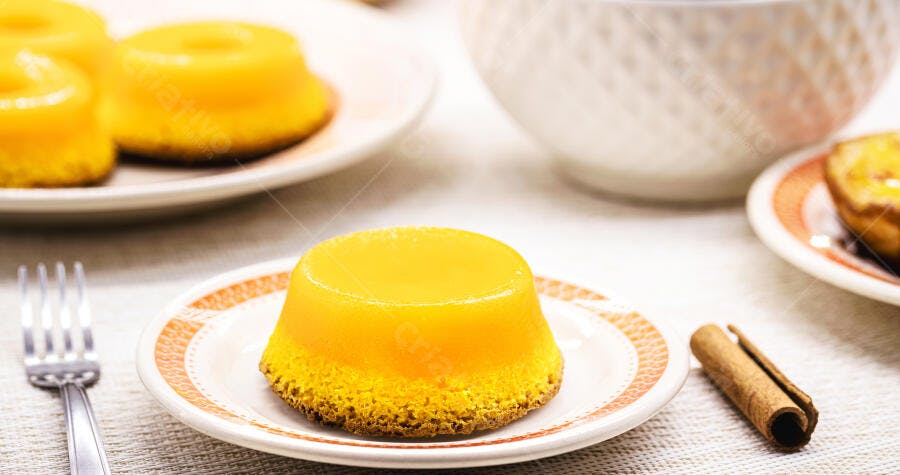 Quindim amarelo brilhante em prato com pau de canela e talheres