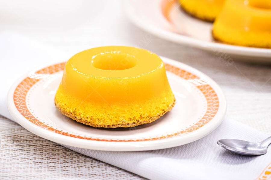 Pudim de milho amarelo brilhante em prato branco com borda laranja sobre mesa