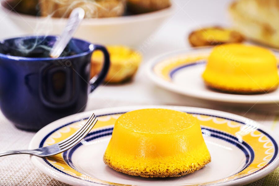 Quindim amarelo em prato decorado com xícara de café fumegante