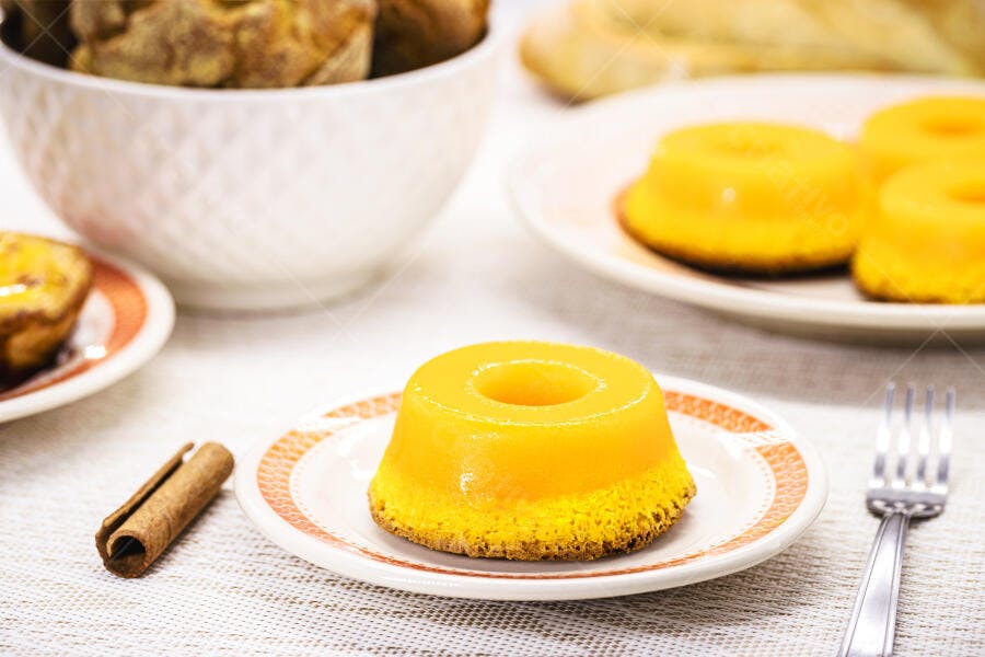 Quindim amarelo brilhante em prato branco com canela e doces na mesa de café