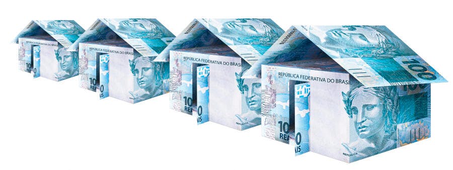 Casas feitas de notas de Real brasileiro R$10 e R$100 em fundo branco abstrato