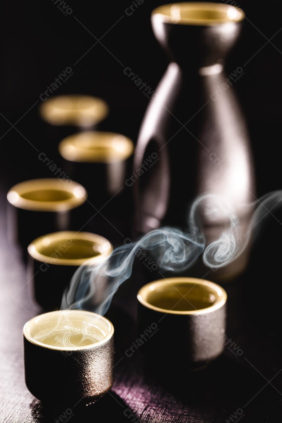 Conjunto de saquê japonês com copos pretos licor quente e fumaça em fundo escuro