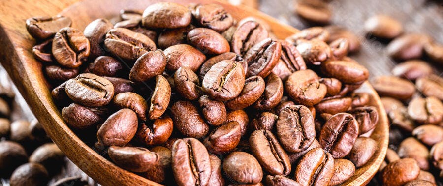 Grãos de café torrados em colher de madeira rústica e fundo desfocado