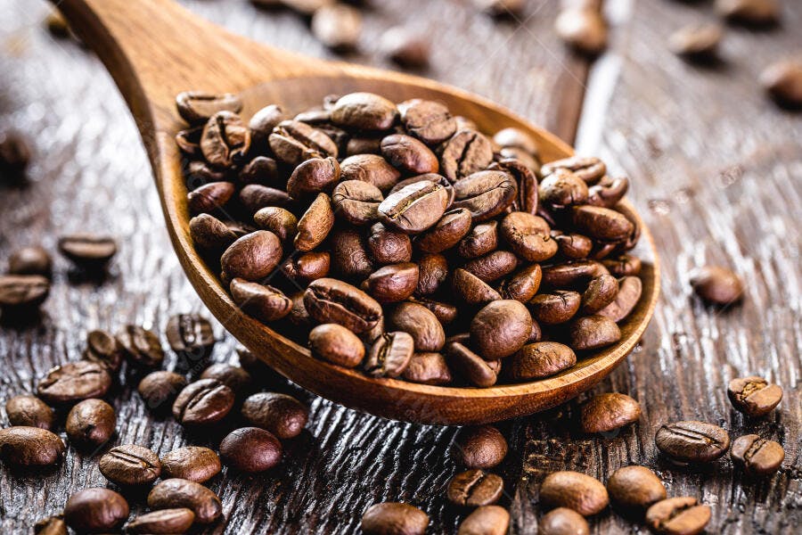 Grãos de café torrados em colher de madeira sobre mesa rústica